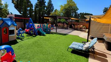 A children's play area with a slide, climbing structures, and a small house.