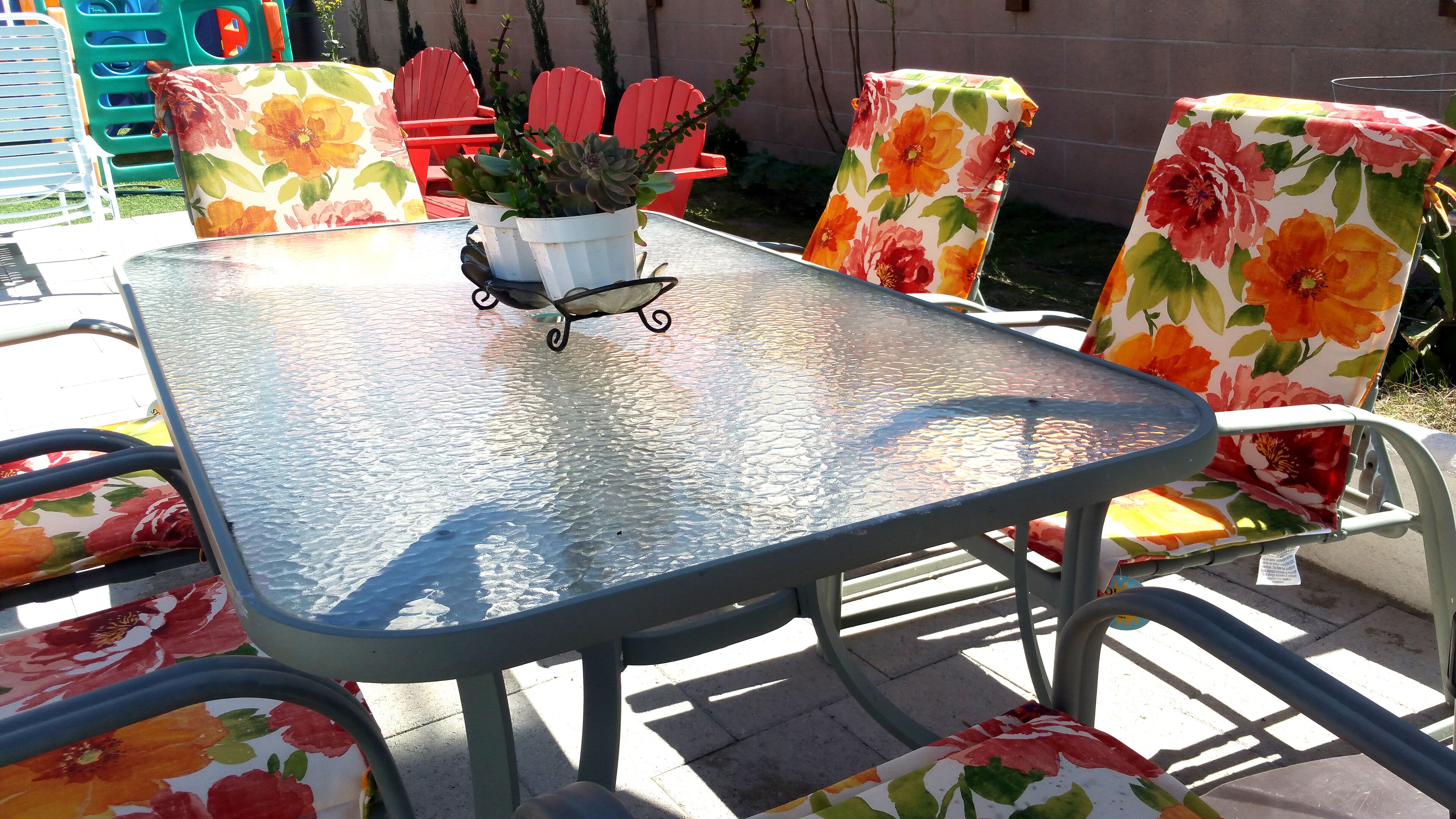Une table en métal recouverte d’une nappe à motifs floraux, entourée de chaises dont le revêtement est également orné de motifs floraux similaires.