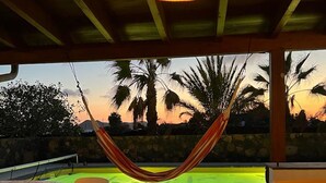 An outdoor patio with a hammock, a round table, and chairs, overlooking a pool and palm trees at sunset. - VILLA VOLCANO- Rural peaceful Gem under the Volcano  (LAJARES)