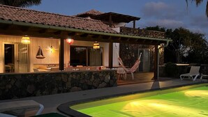 A poolside area with lounge chairs, a hammock, and a house with a tiled roof and stone walls. - VILLA VOLCANO- Rural peaceful Gem under the Volcano  (LAJARES)