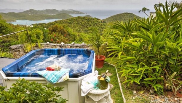 A hot tub surrounded by lush greenery, with a view of hills and a body of water in the background. - Fantastic Panoramic Views of The British Virgin Islands, Amazing Sunrises, Pool  (Coral Bay)
