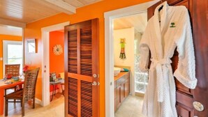 A room with orange walls, a wooden door, a white robe hanging on the door, and a dining area with a table and chairs. - Fantastic Panoramic Views of The British Virgin Islands, Amazing Sunrises, Pool  (Coral Bay)