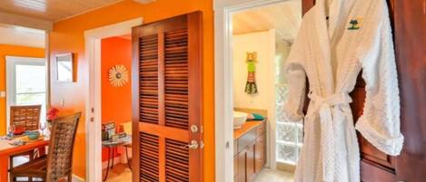 Une pièce aux murs orange, une porte en bois, une robe blanche accrochée à la porte et un coin repas avec une table et des chaises.