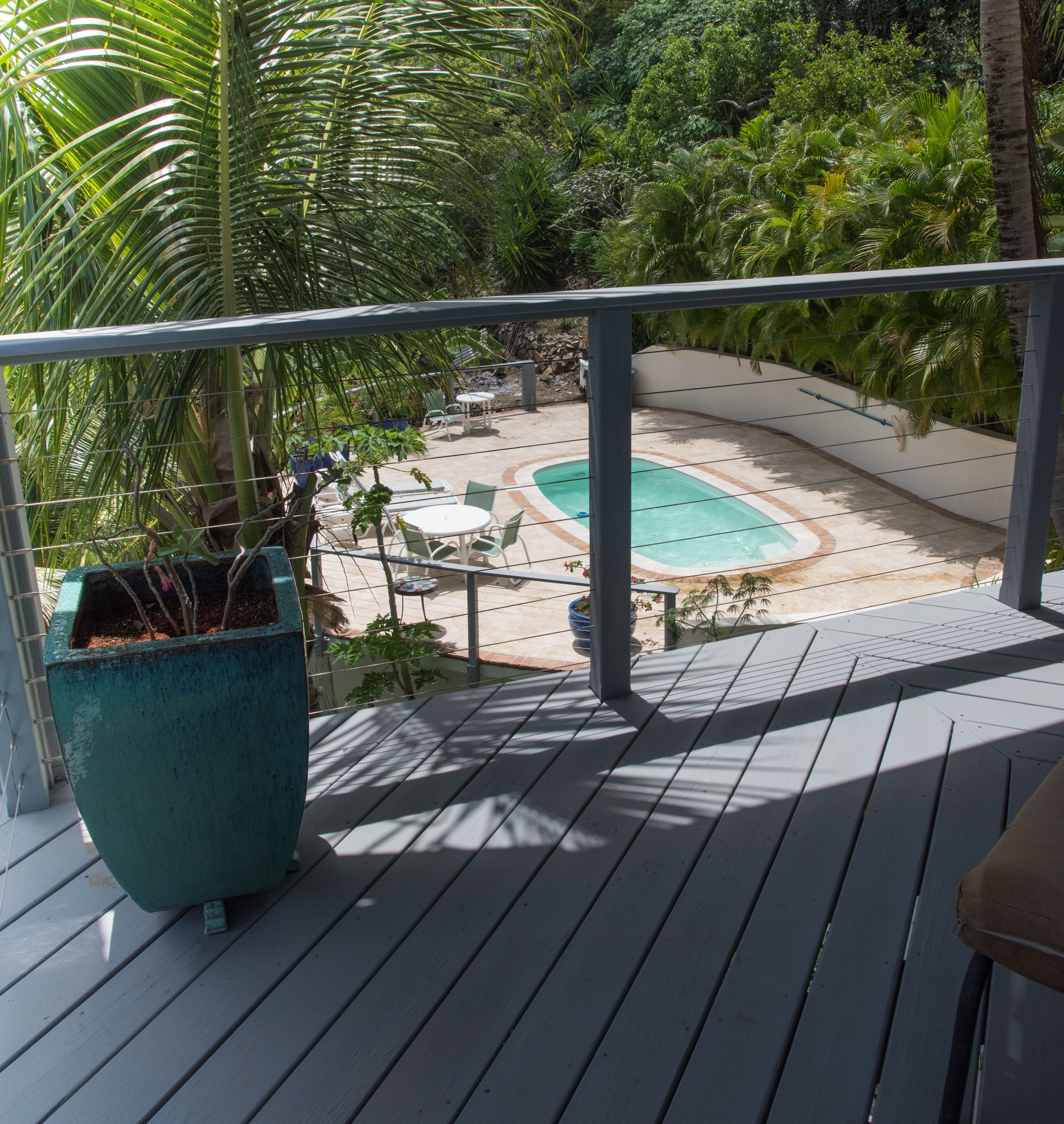 A wooden deck with a pool, surrounded by lush greenery and a stone wall.