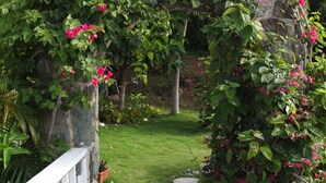 A stone archway with pink flowers, a wooden deck, and a grassy garden. - Fantastic Panoramic Views of The British Virgin Islands, Amazing Sunrises, Pool  (Coral Bay)