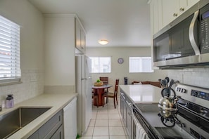 A modern kitchen with white cabinets, a stainless steel refrigerator, a microwave, and a kettle on the stove.