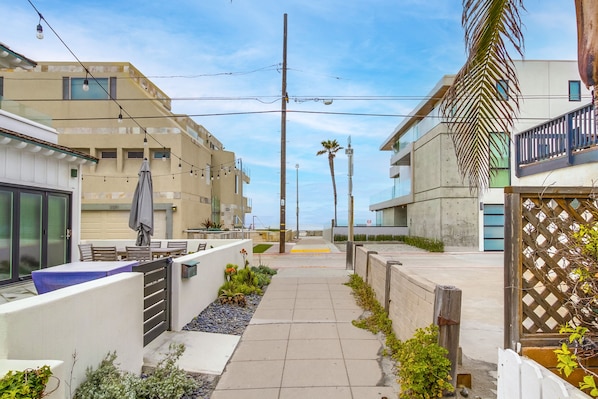 A narrow pathway flanked by modern buildings with balconies, a clear sky, and outdoor seating areas.