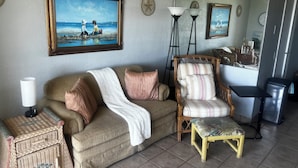 Un salon avec un canapé, un fauteuil, des paniers en osier, une lampe et un tableau accroché au mur.