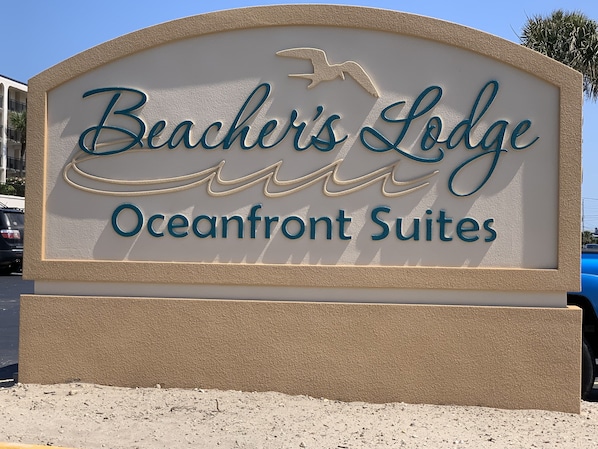 A sign for Beacher's Lodge Oceanfront Suites with a bird silhouette and wavy lines. - Oceanfront! Panoramic Views- Heated Seaside Pool - Private Balcony on 2nd Floor  (Crescent Beach - St Augustine)