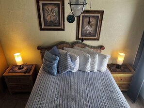 Una cama con ropa de cama a rayas, dos mesitas de noche con lámparas y dos cuadros en la pared.