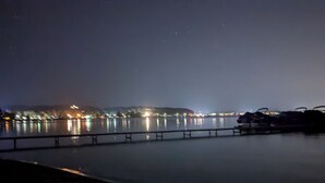 A nighttime view of a waterfront area with a bridge, illuminated buildings, and a calm body of water. - Make memories on Grand Traverse East Bay. (Williamsburg)