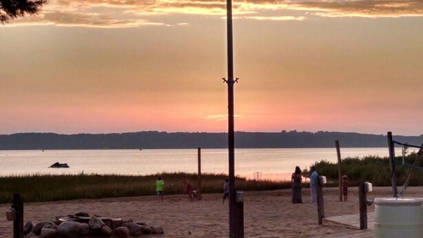 A beach with a sunset, a volleyball net, and people playing. - Make memories on Grand Traverse East Bay. (Williamsburg)