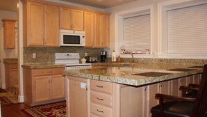 Una cocina con armarios de madera, encimera de granito, microondas integrado, cafetera y ventana con persianas.