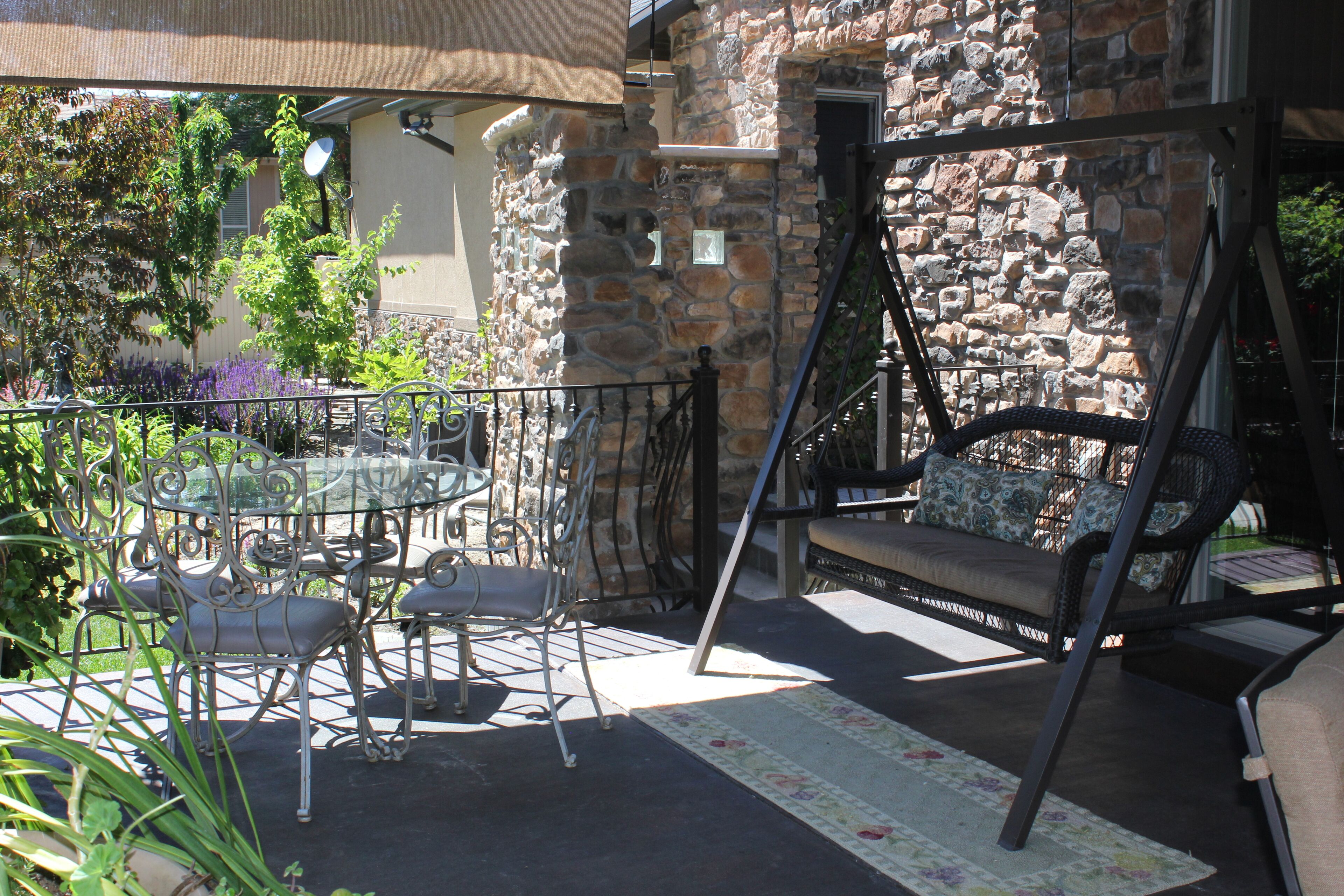 An outdoor patio with a stone wall, a swing chair, a dining table with chairs, and a metal fence.