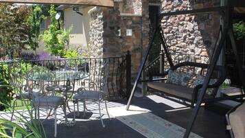 An outdoor patio with a stone wall, a swing chair, a dining table with chairs, and a metal fence.