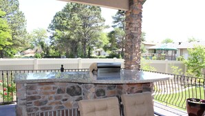 Un patio exterior con barra de piedra y vidrio, dos sillones acolchados y una planta en maceta.