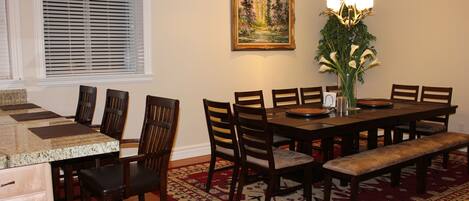 Un coin repas comprenant une table en bois, des chaises, un banc, un tapis, un tableau et un lustre.