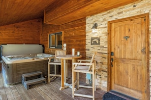 A wooden cabin with a hot tub, a small table with chairs, and a stone wall with a door. - Large Cabin w/Hot Tub, Great Views, Gas Fireplace,Game Room w/Air Hockey,Firepit (Angel Fire)