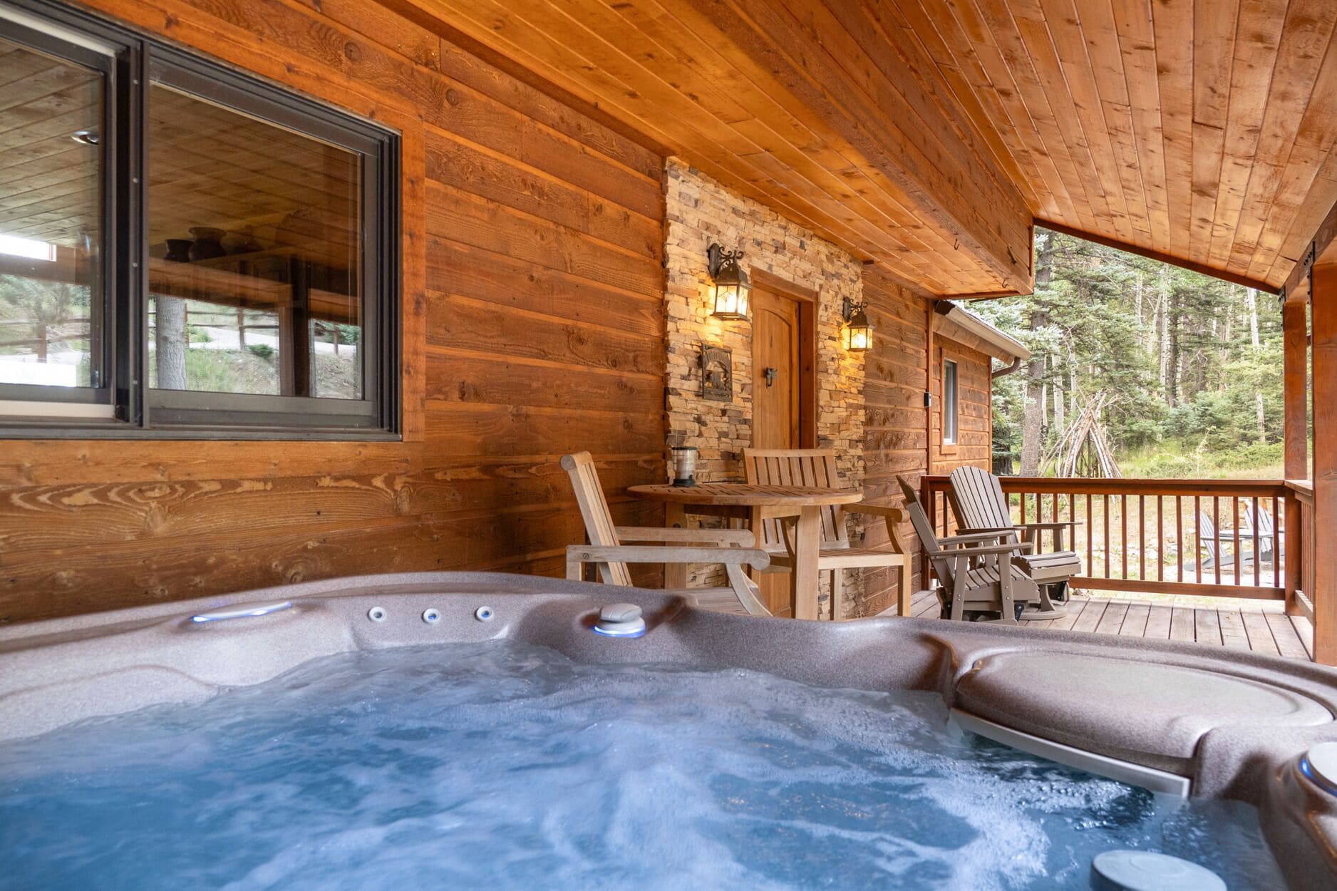 A wooden cabin with a hot tub, wooden deck, and stone walls.