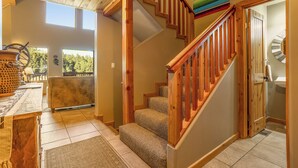 Una escalera de madera con peldaños alfombrados que conduce a un segundo piso. En primer plano, se ve una mesa de madera rústica con una cesta tejida.