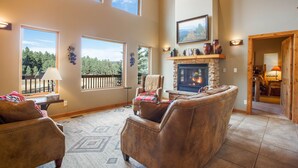 Un salón amplio con sofás de cuero, chimenea de piedra, ventanas grandes y vistas al exterior.