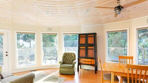 A spacious room with large windows, a ceiling fan, a dining table with chairs, and a green armchair.