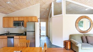 A modern kitchen with wooden cabinets, a microwave, and a refrigerator. There is a dining table with chairs and a sofa with a mirror.
