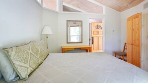 A bedroom with a bed, a nightstand, a lamp, a wooden wardrobe, and a door leading to another room.