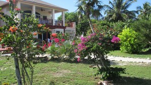 A two-story house with a balcony, surrounded by lush greenery and flowering plants. - EXCLUSIVE PROPERTY BEACHFRONT CONDO 3bed/3Bath DIRECTLY on beautiful HOOPERS BAY (Georgetown)