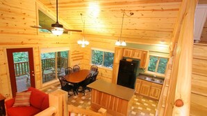 A wooden cabin interior with a dining area, kitchen, and a red sofa.