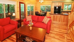 A wooden cabin interior with a red sofa, a dining table, and a kitchen area.