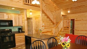 A wooden cabin interior with a kitchen, dining area, and staircase.