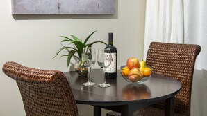 A dining table with two wine glasses, a bottle of wine, and a bowl of fruit. - Paradise @ Sapphire Village Studio- H-S WIFI -No Excess Owner Fees #307 (St Thomas)