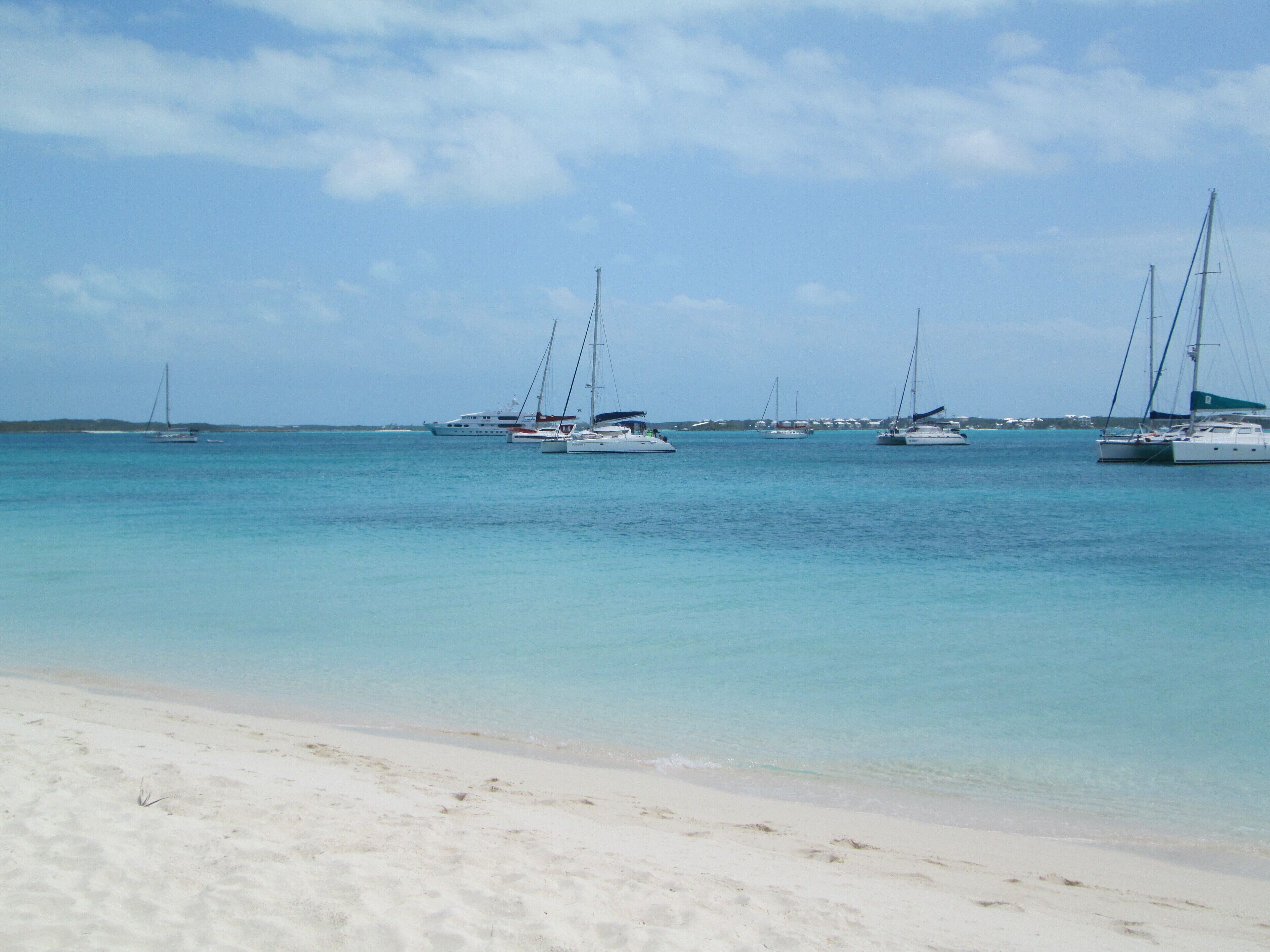 A beach with several sailboats anchored in calm waters.
