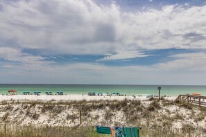Ein Strand mit Sonnenschirmen und Liegestühlen, eine Holzumzäunung und freier Blick auf das Meer.