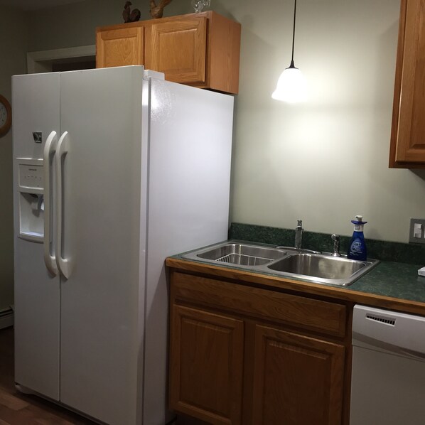 A kitchen with a white refrigerator, wooden cabinets, a stainless steel sink, and a blue Dawn dish soap bottle.