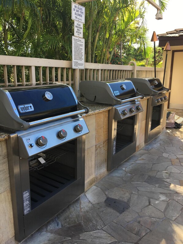 Un barbecue équipé de plusieurs brûleurs et d’un four intégré, installé à l’extérieur, avec une clôture en bois et une végétation luxuriante en arrière-plan.
