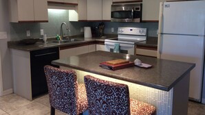 A modern kitchen with a central island, stainless steel appliances, and patterned chairs. - SALE! -- Best Location  &  Closest to the Beach - One Bedroom (kihei)
