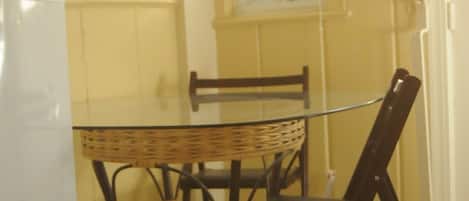 A dining area with a glass table, wicker chairs, and a white refrigerator.