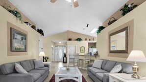 A spacious living room with two grey sofas, a white coffee table, and a red rug. There are two lamps, a framed picture, and a mirror on the walls. - Upscale Home, Pool, Hot Tub, EV Charger, Pets OK, 10% Off Golf Cart Rentals (Miramar Beach)
