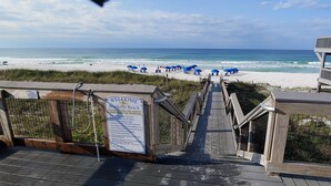 A wooden boardwalk leading to a beach with blue umbrellas and a signboard. - Upscale Home, Pool, Hot Tub, EV Charger, Pets OK, 10% Off Golf Cart Rentals (Miramar Beach)