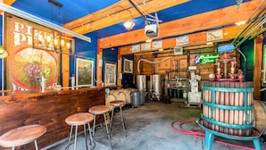 Una zona de bar rústica con vigas de madera, una barra con taburetes y diverso equipo de elaboración de cerveza.