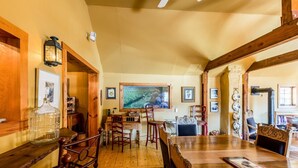 Un comedor amplio con mesas y sillas de madera, obras de arte en las paredes y un gran ventanal que proporciona luz natural.