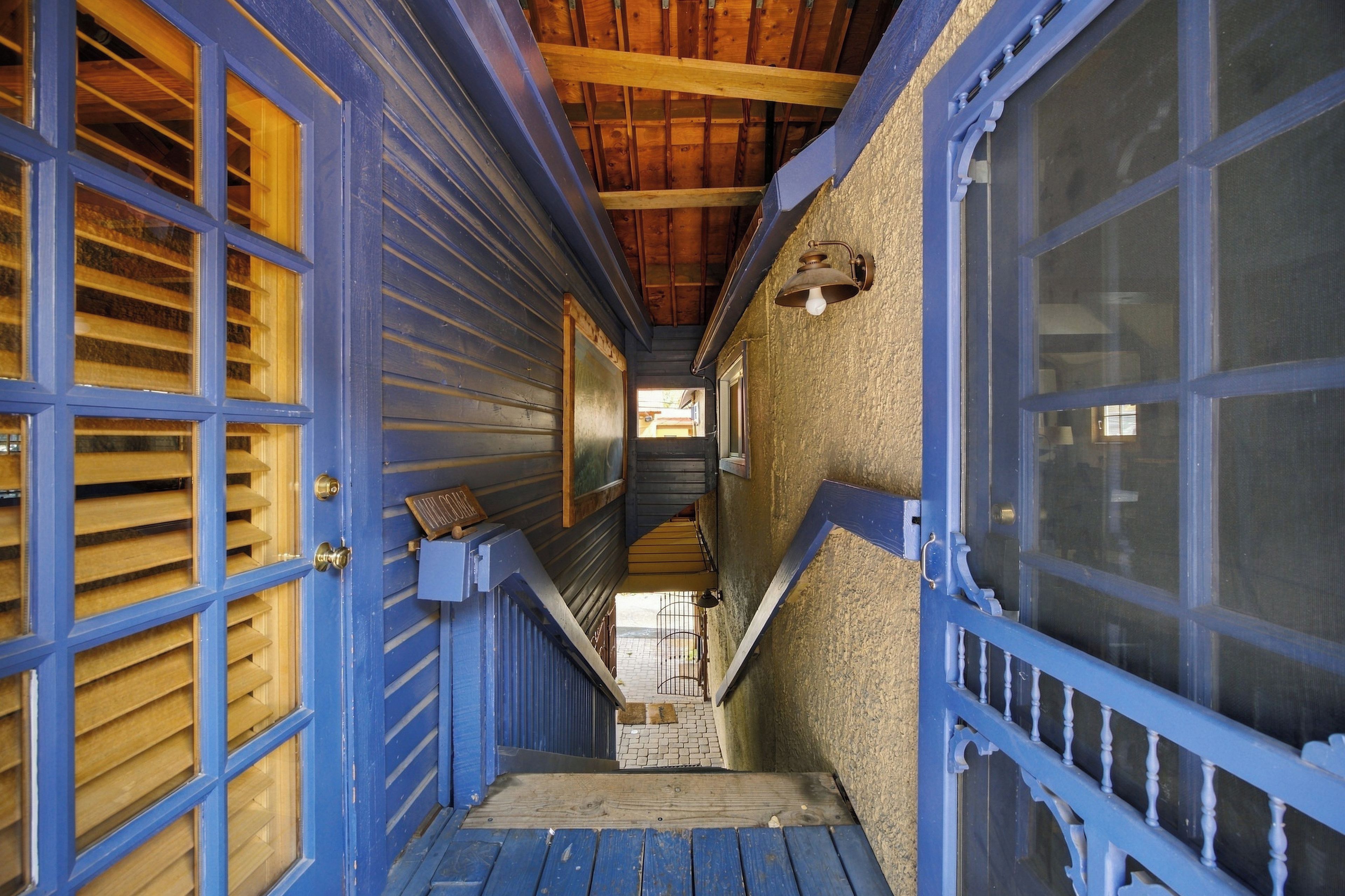 A narrow hallway with blue doors and wooden shutters, leading to a staircase.