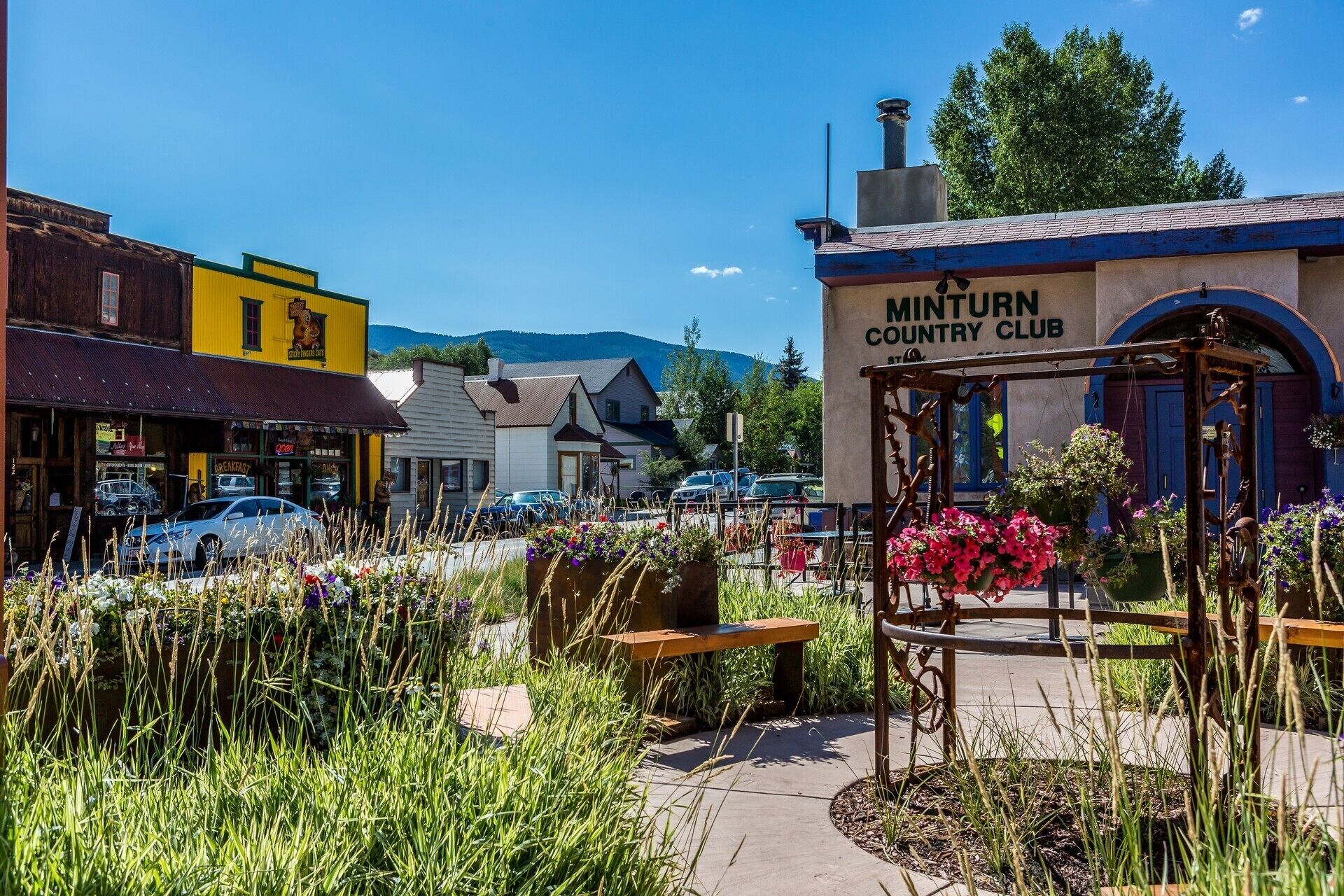 A country club with a sign, surrounded by a garden with benches and flowers.