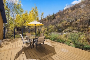 A wooden deck with a glass-top table and chairs, surrounded by trees with yellow leaves. - Beautiful & One-of-a-Kind Downtown Minturn - Minutes to Vail (Minturn)