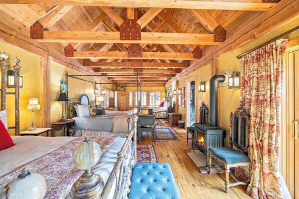 A cozy room with a bed, a blue upholstered bench, a fireplace, and wooden beams on the ceiling. - Beautiful & One-of-a-Kind Downtown Minturn - Minutes to Vail (Minturn)