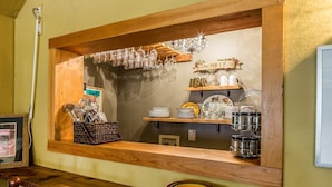 Una cocina con estantes de madera, un ventanal con copas de vino colgando, y un letrero que dice 'En el vino reside la verdad'.