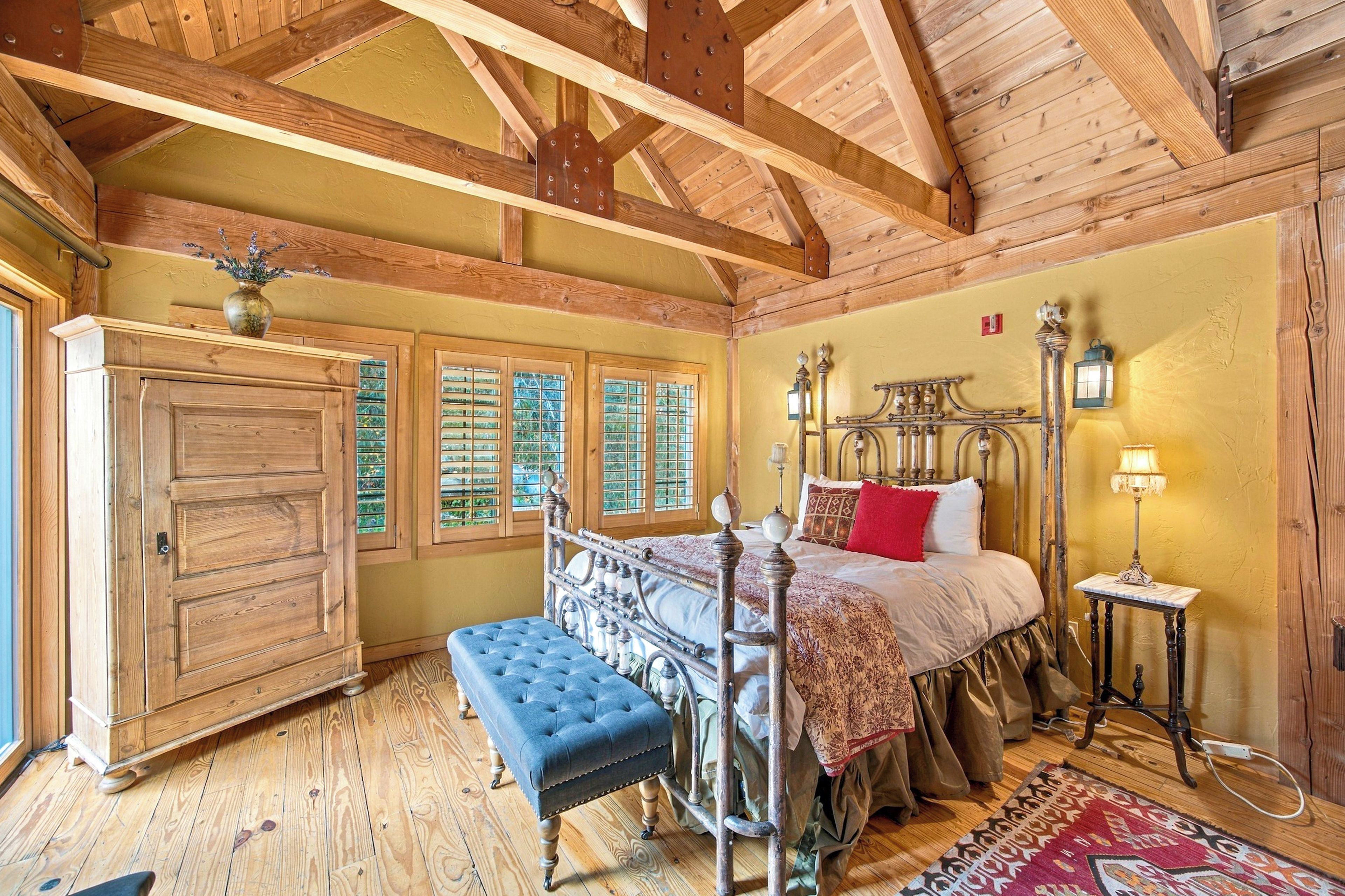 Una habitación tradicional con techo de madera, una cama con estructura metálica, un banco y un armario.