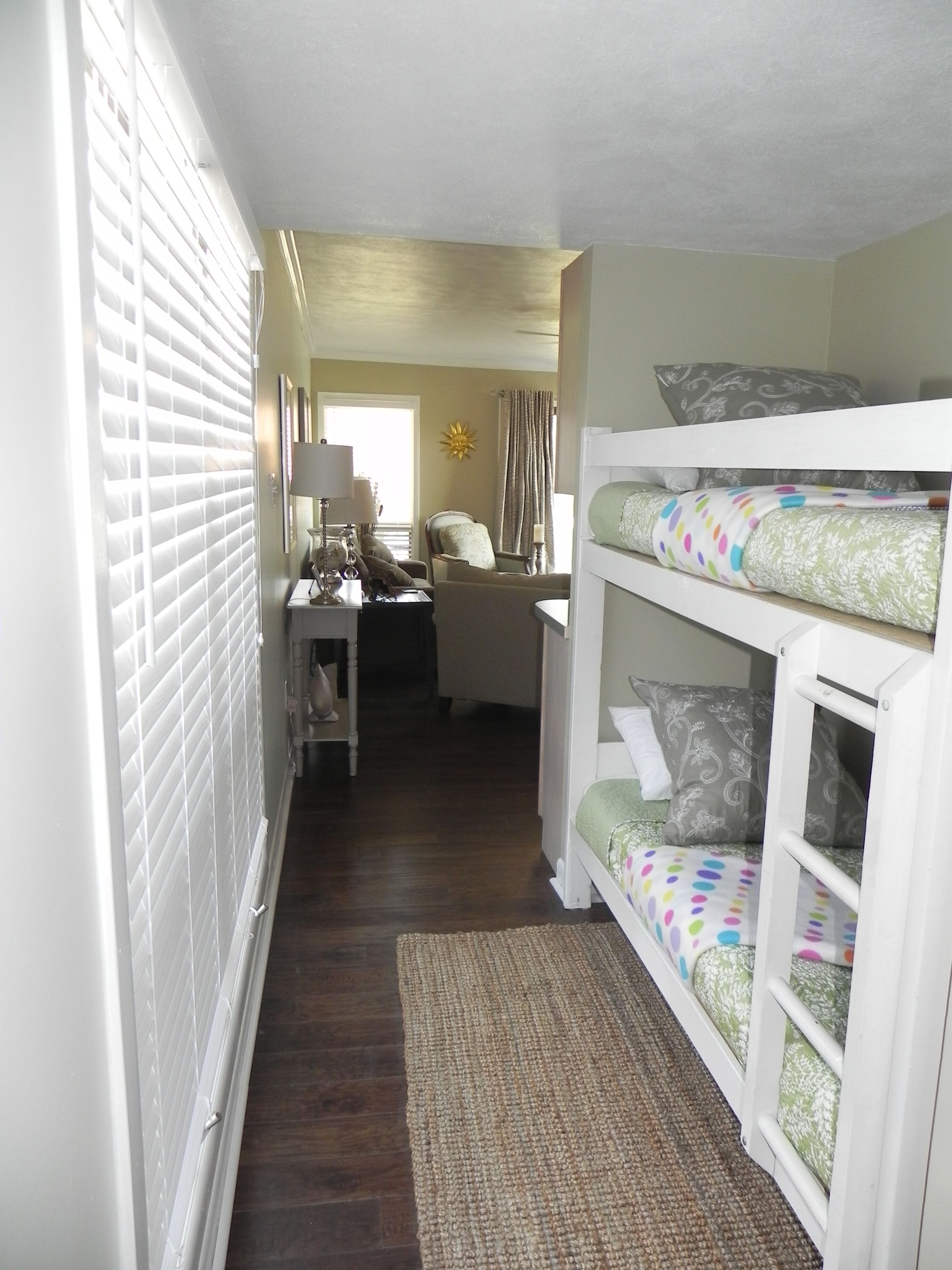 A narrow hallway with a bunk bed on the right, a chair in the center, and a lamp on a nightstand.